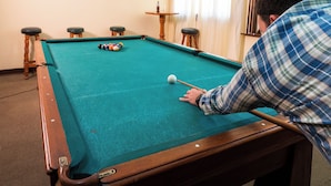 Een pooltafel met ballen, een keu en een ingelijst kunstwerk aan de muur.