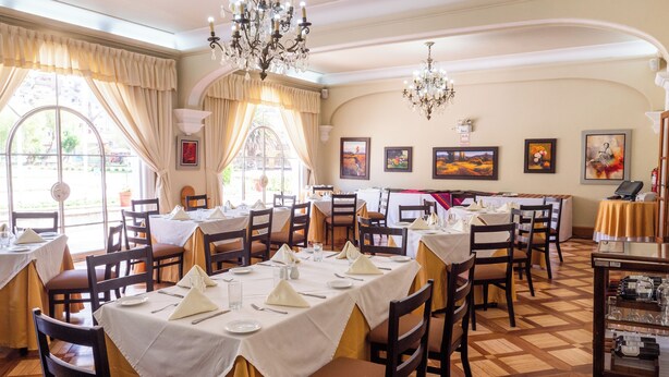 Een restaurant met meerdere tafels klaar voor diners, met een zwart-wit schaakbordvloer, houten stoelen en een kroonluchter.
