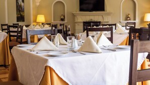 Een eetruimte met gedekte tafels, compleet met witte tafelkleden, servetten en glazen.