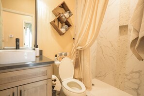 Ein Badezimmer mit Toilette, Holzregal mit Handtüchern, Spiegel und Duschvorhang.
