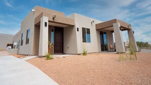 A modern two-story house with a flat roof, large windows, and a gravel driveway.