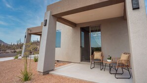 A modern building with a covered patio area featuring two wicker chairs and a small table.
