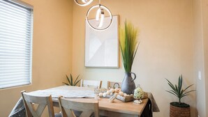 A dining area with a wooden table, chairs, a vase with green plants, a pitcher, and decorative items.
