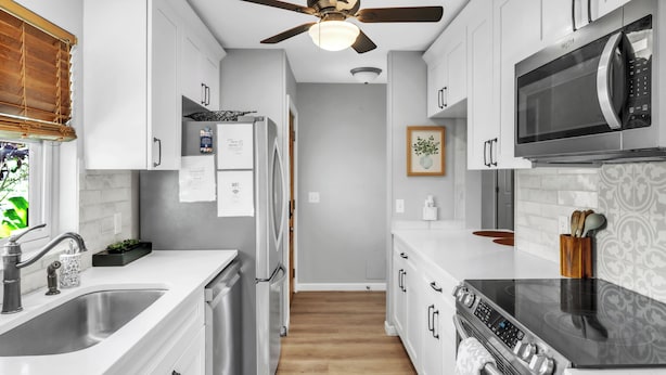 Una cocina moderna con armarios blancos, un refrigerador de acero inoxidable, un microondas y una estufa negra.