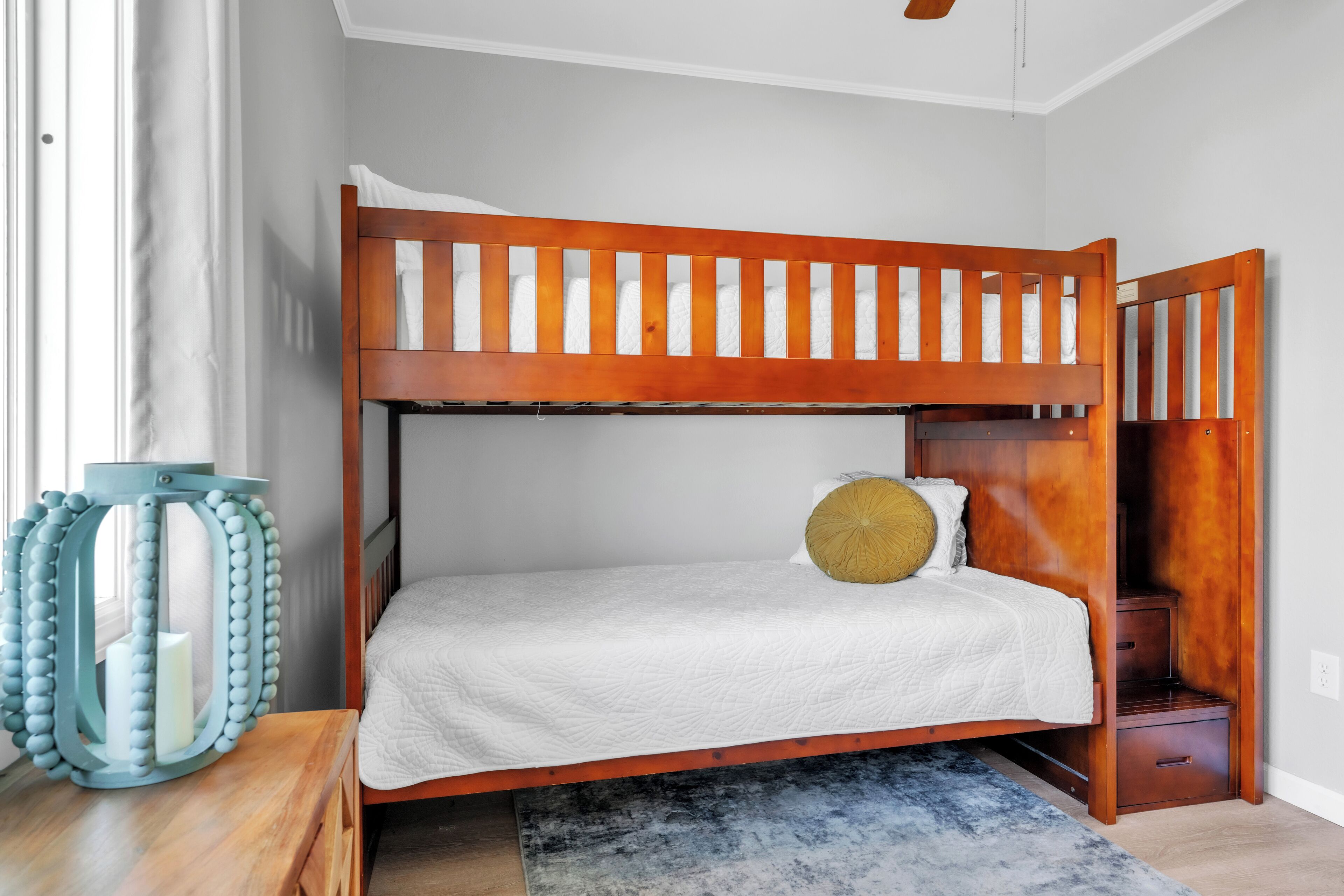 A bunk bed with a wooden frame, a white quilted mattress, and a small wooden nightstand with drawers.