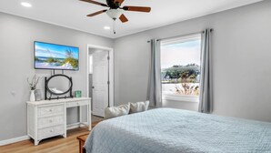 Un dormitorio con cama, cómoda, ventilador de techo, televisor y ventana con cortinas.