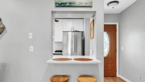 Una cocina con nevera de acero inoxidable, taburetes de madera y encimera blanca.