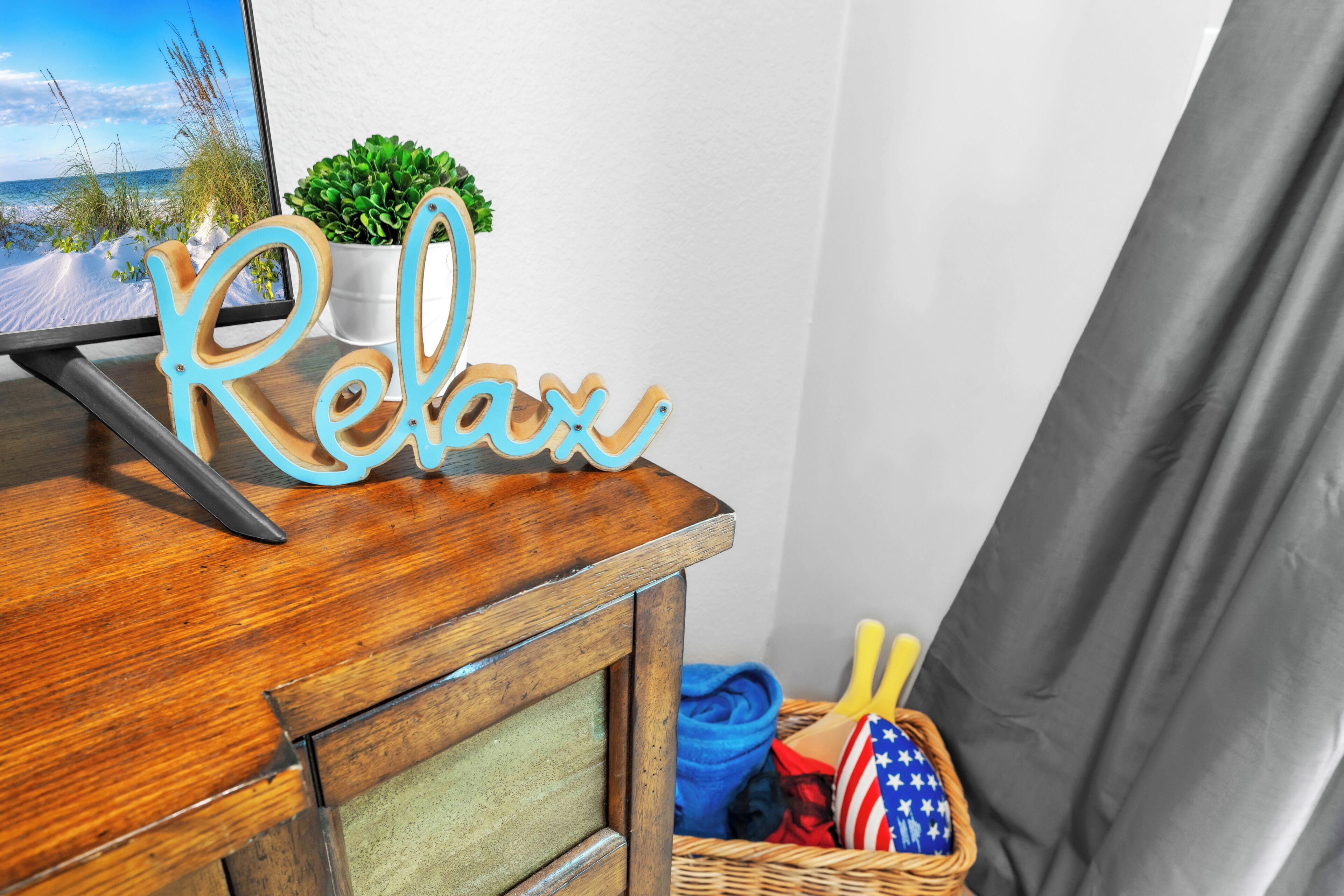 Ein Holztisch mit einem 'Relax'-Schild, einem Computer, einer Topfpflanze und einem Korb mit einer gefalteten US-amerikanischen Flagge und gelben Gegenständen.