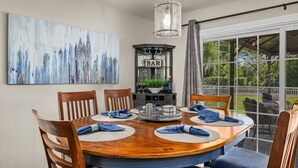 Un coin repas avec une table ronde en bois, six chaises et une enseigne de bar.