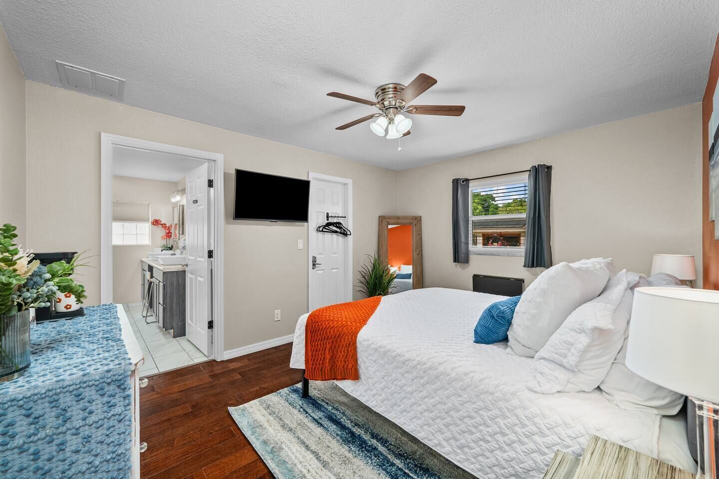 A modern hotel room with a bed, a ceiling fan, a TV, and a bathroom visible through an open door.