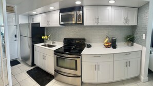 Una cocina moderna con armarios blancos, un refrigerador de acero inoxidable, una estufa negra, un microondas y una cafetera Keurig.