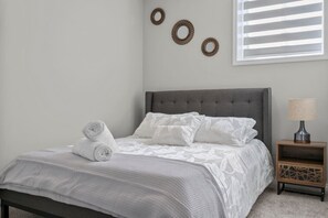 Una cama bien hecha con cabecera gris, una mesita de noche con lámpara, y tres anillos decorativos en la pared.