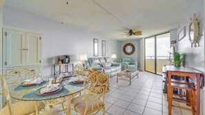 A spacious living area with a dining table set for four, a sofa, and a ceiling fan.