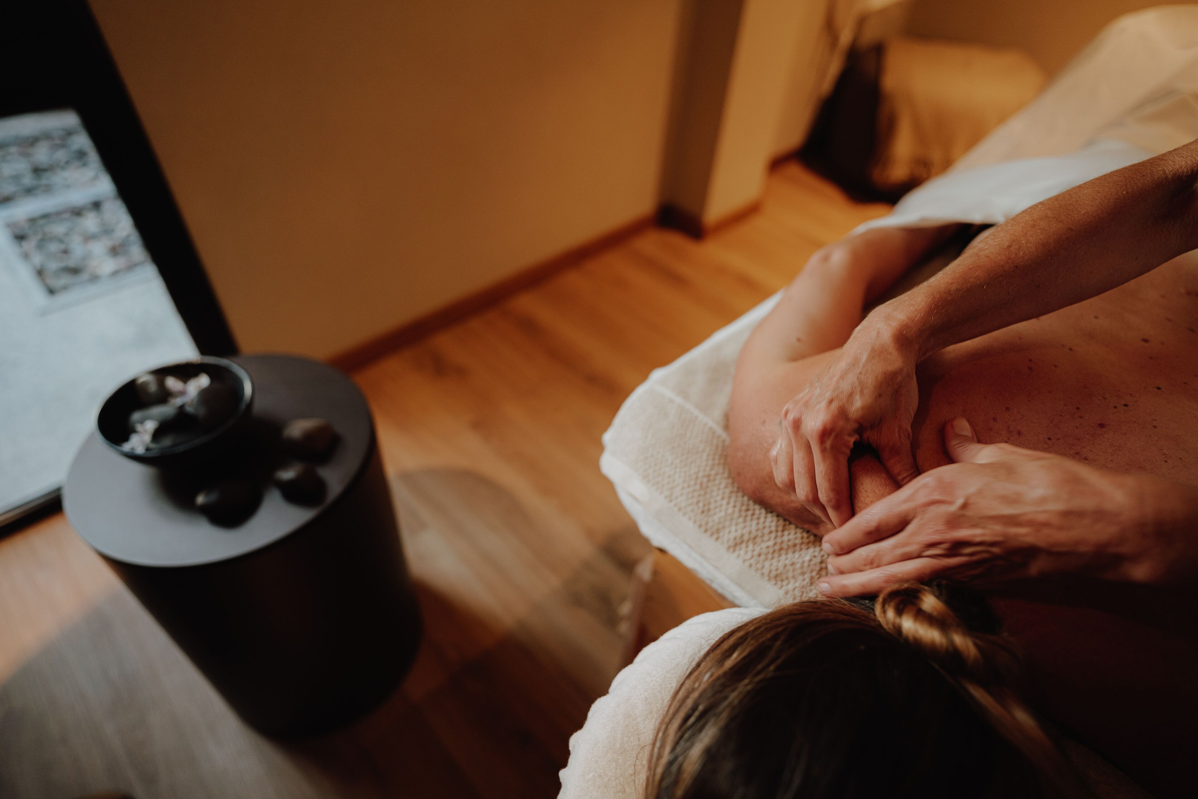 Een massagetherapie sessie in een ruimte met houten vloeren en een massagetafel.