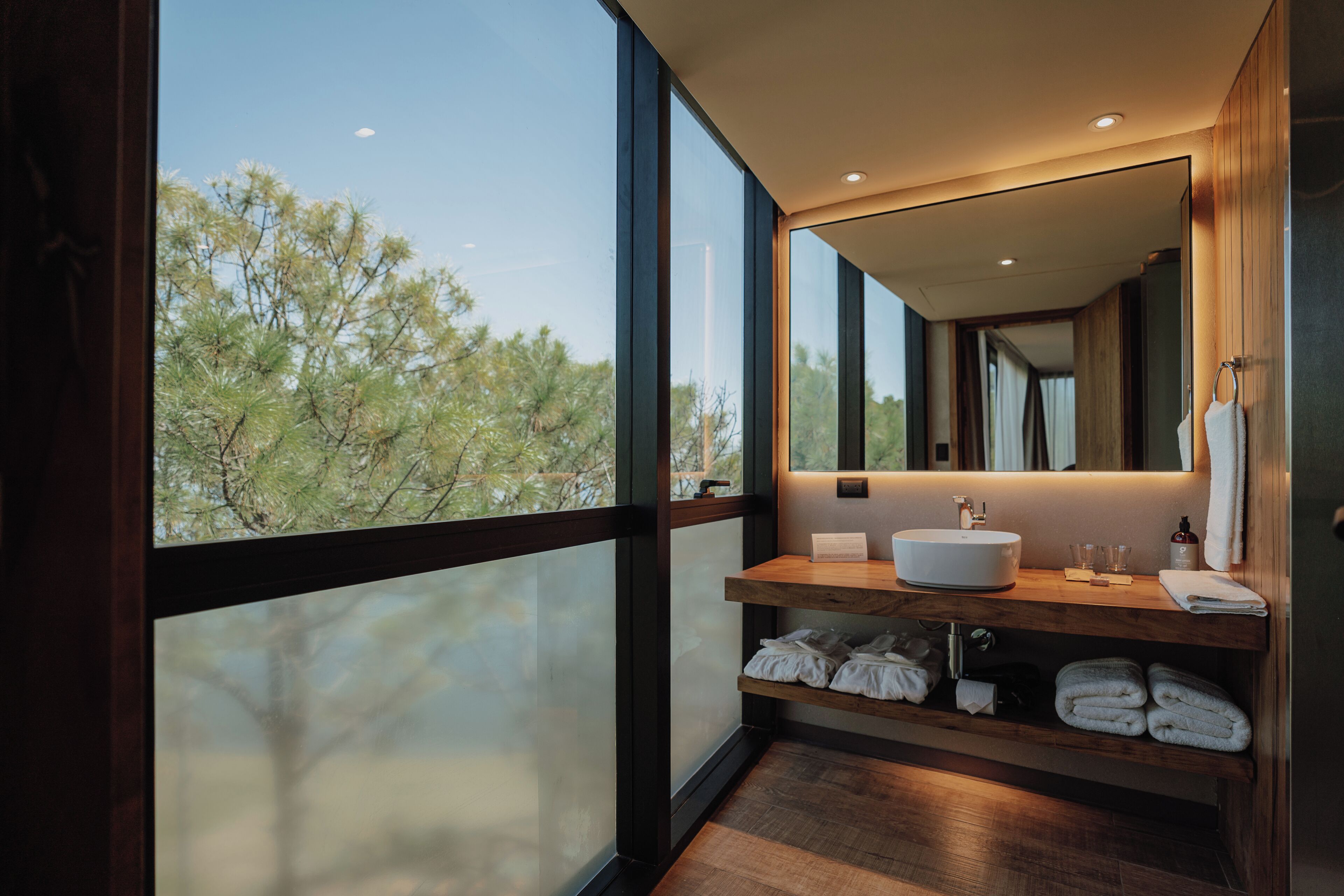 Un baño moderno con un ventanal grande, tocador de madera y un espejo.