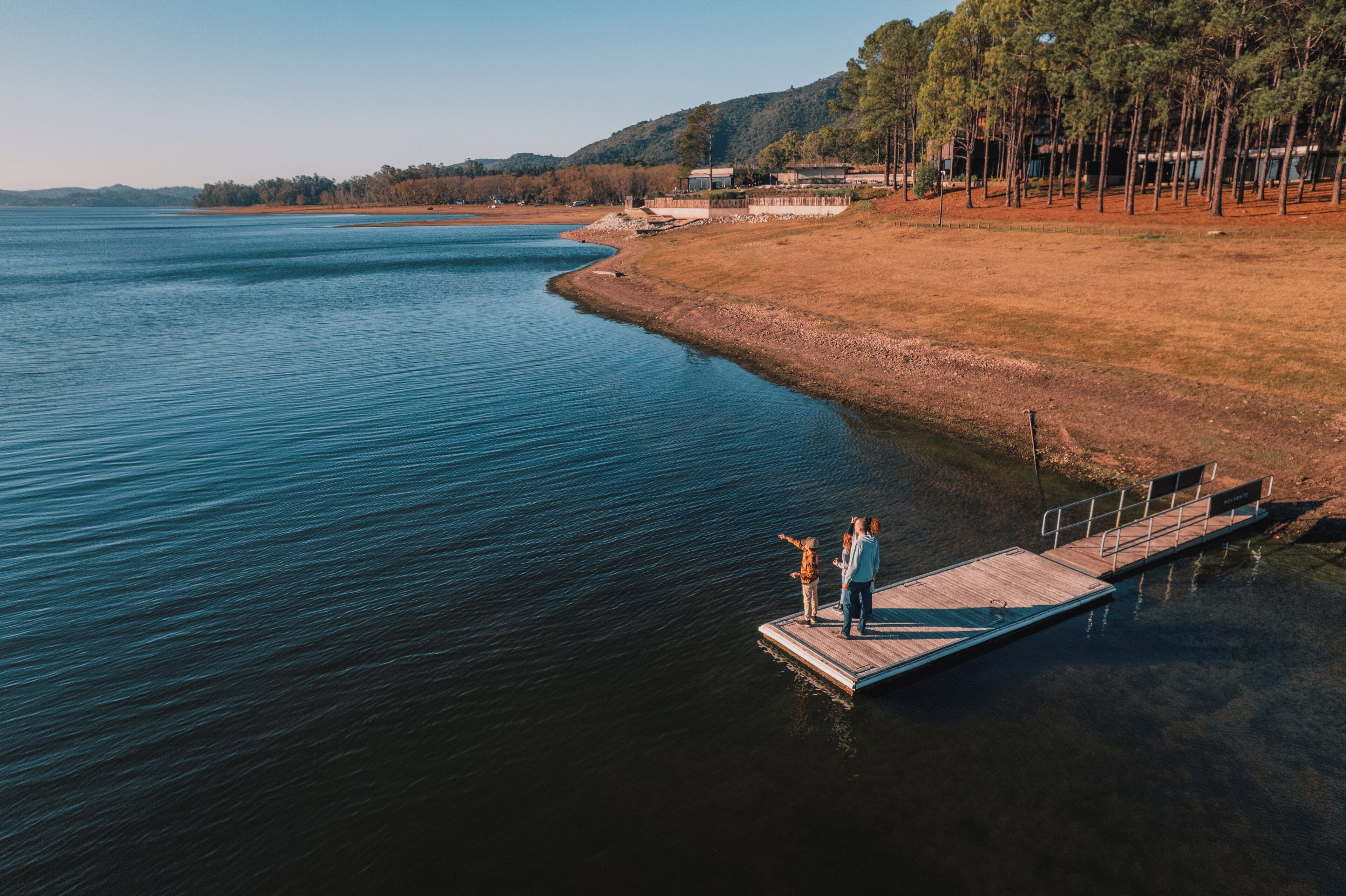A wooden dock extending into a calm lake with two people standing at the end.