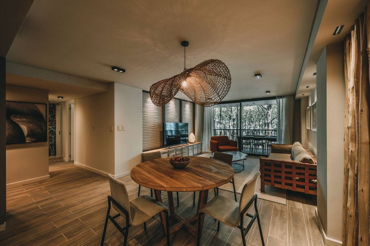 A modern dining area with a round wooden table, four chairs, and a hanging light fixture.