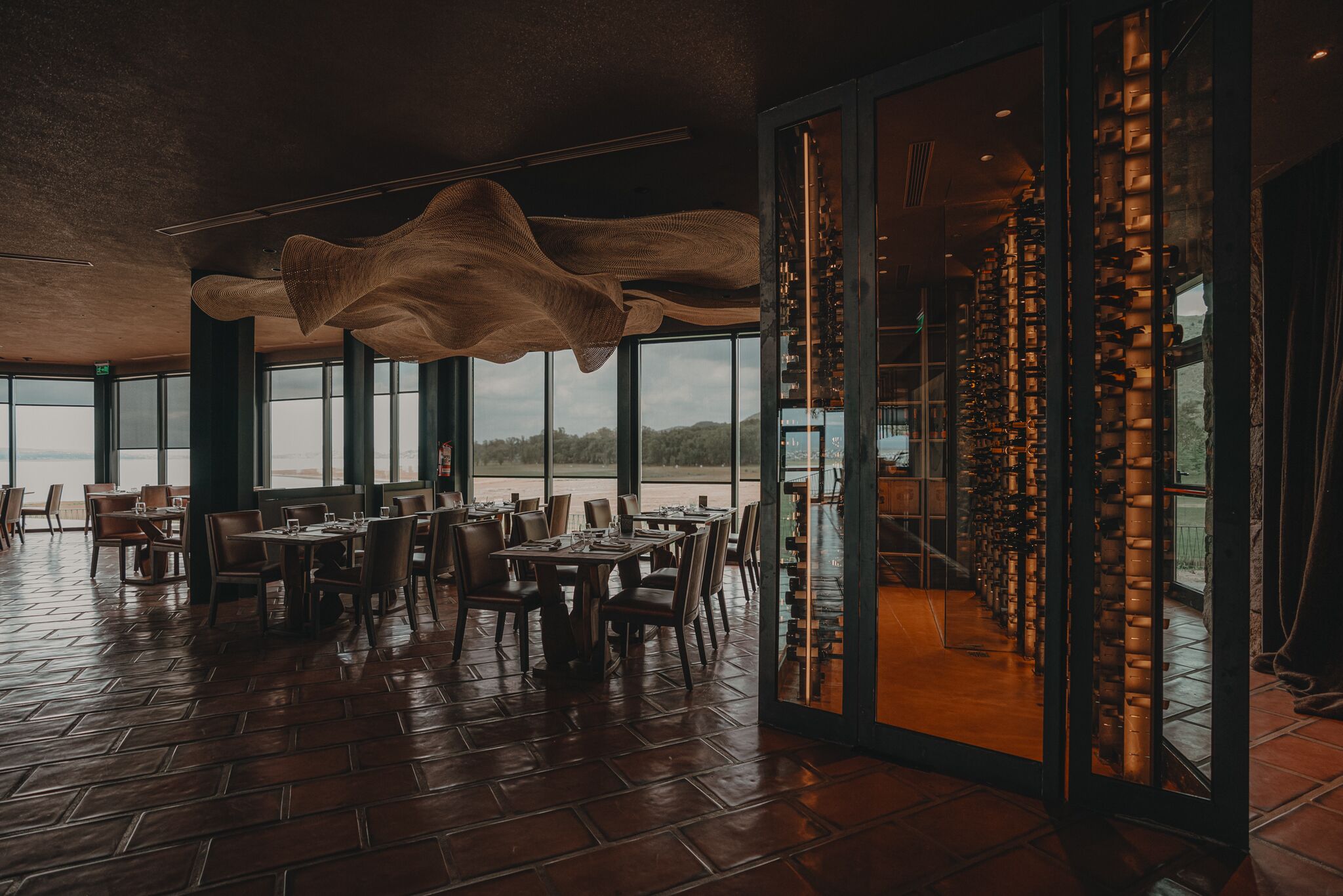 A restaurant with a view of the water, large windows, and a unique hanging light fixture.