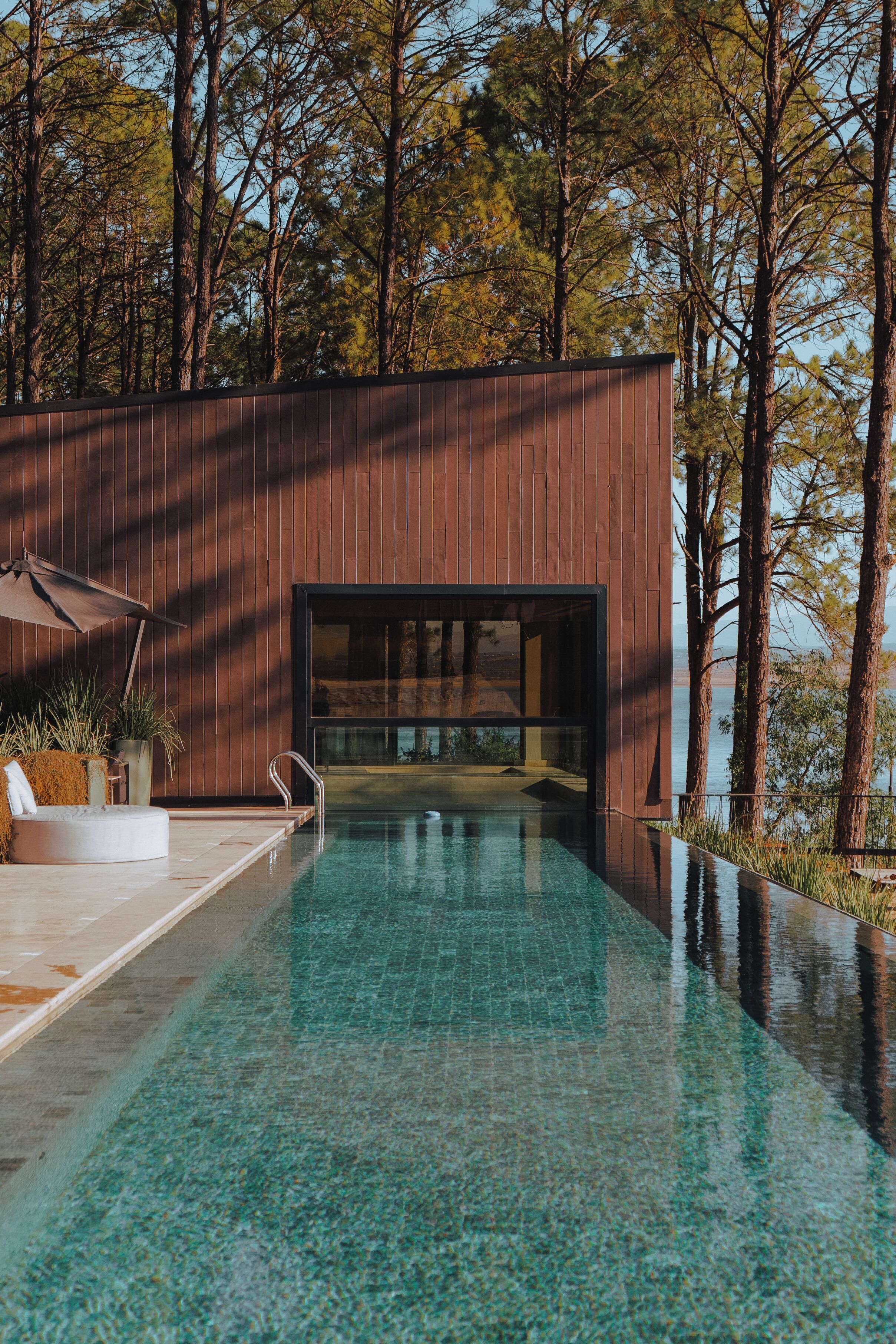 Zona de piscina moderna amb un solàrium de fusta, gandules i vistes a la forest circumdant.