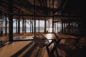 Un comedor moderno con una mesa grande y sillas de mimbre, con vistas a una playa y al mar.