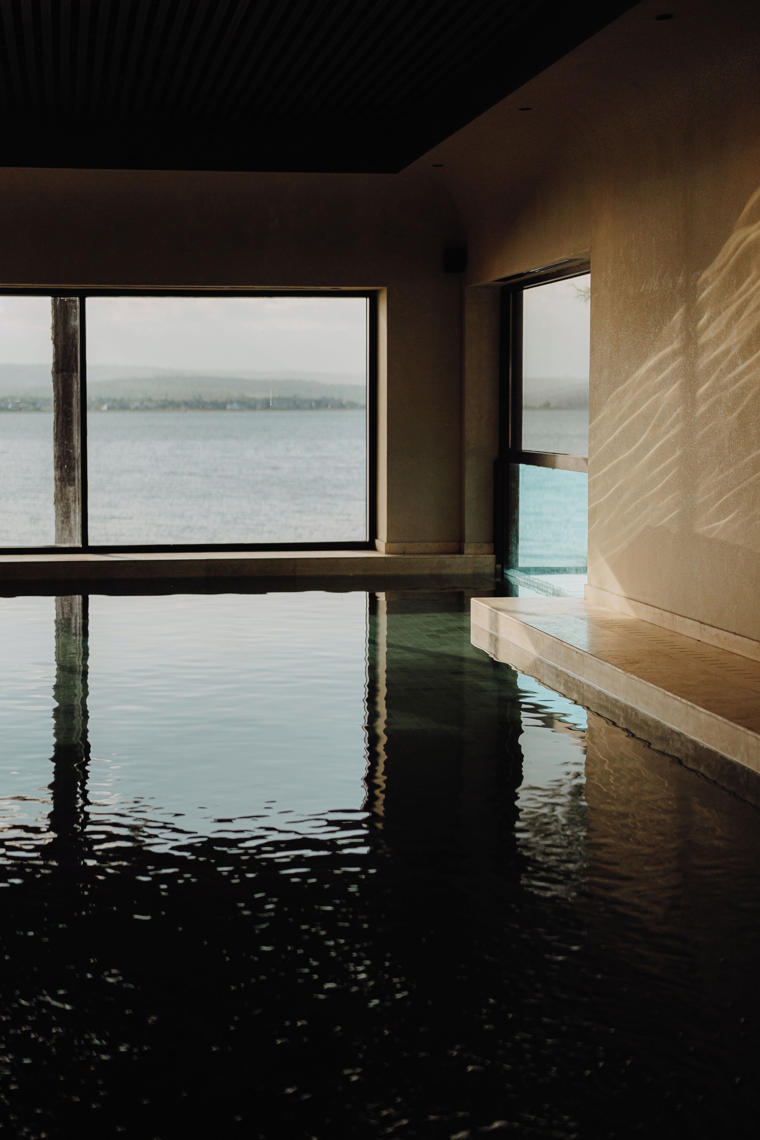 An indoor swimming pool with large windows overlooking a body of water.