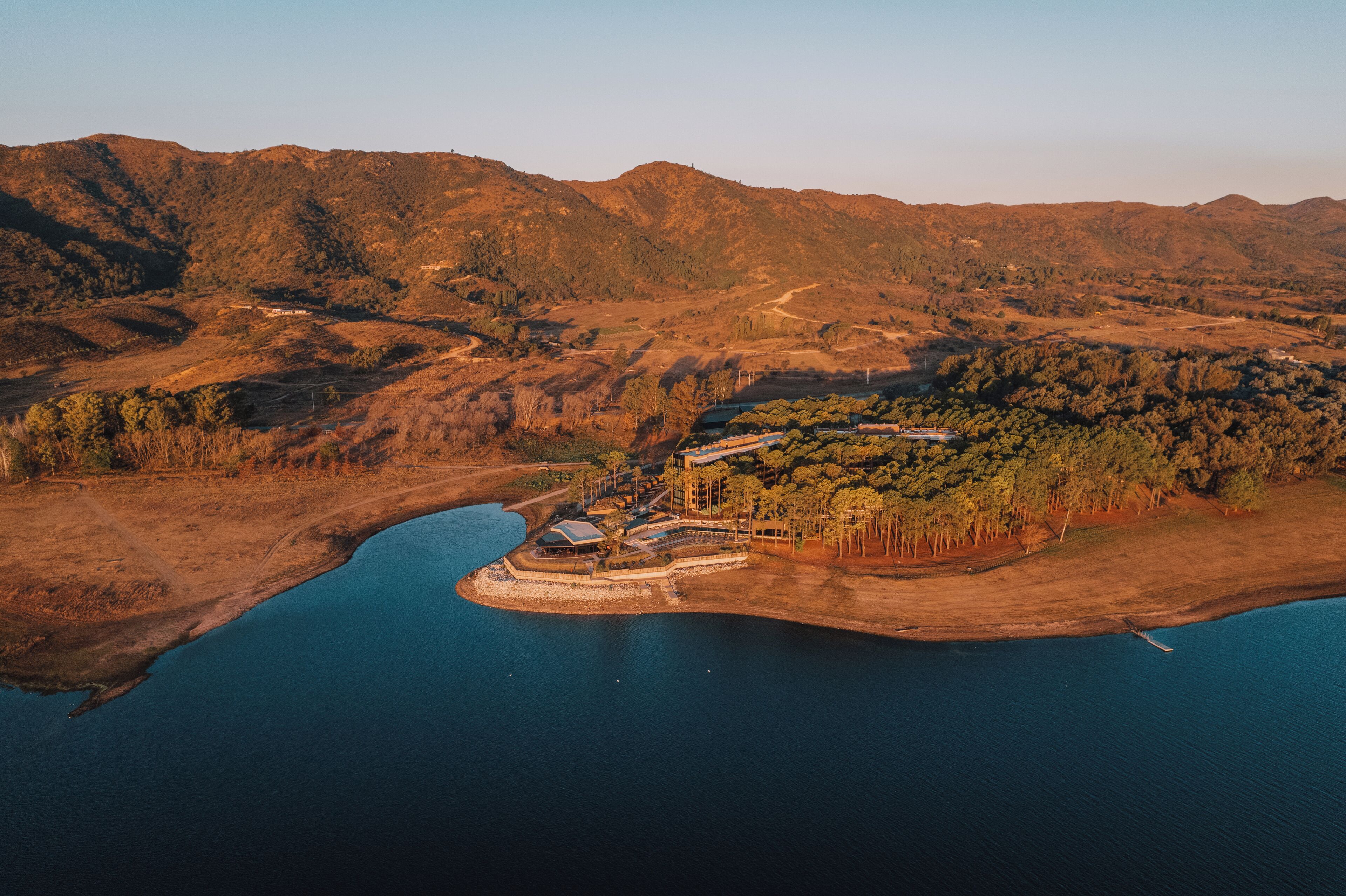 Vista aerea di una proprietà costiera con un'ampia distesa d'acqua, un molo e un complesso di edifici circondato da colline.