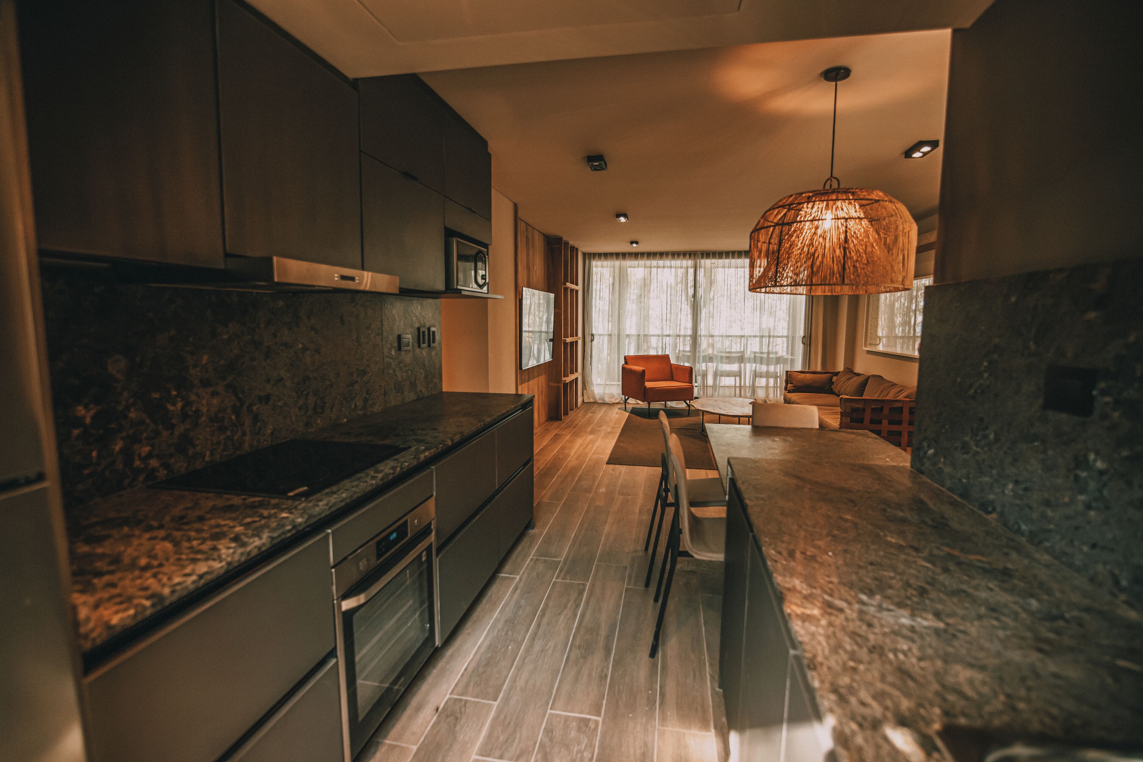 A modern kitchen with granite countertops, stainless steel appliances, and a dining area with a large window and a hanging light fixture.