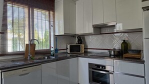 Eine moderne Küche mit weißen Schränken, einem Geschirrspüler, einem Backofen, einer Mikrowelle und einem Fenster mit Jalousien.