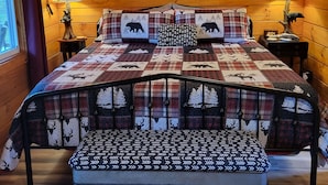 Ein gemütliches Schlafzimmer im Chalet-Stil mit Holzbalkendecke, einer gesteppten Bettdecke, zwei Nachttischlampen und einer Bank am Fußende des Bettes.