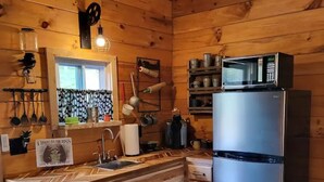 Eine kleine Küche mit Holzausstattung, einem Edelstahlkühlschrank und einem Fenster mit gemusterten Vorhängen.
