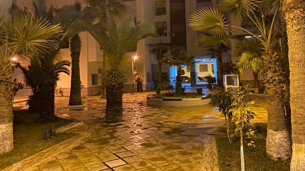 Une cour intérieure agrémentée de palmiers, d’une fontaine et d’un bâtiment dont les fenêtres sont illuminées.