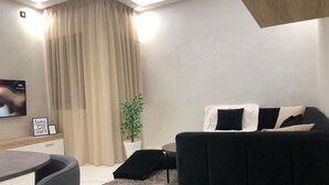 Un salon moderne avec un canapé noir, une petite table, une plante en pot et un téléviseur.