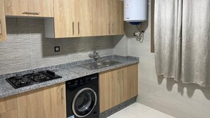 Une cuisine compacte avec des meubles en bois, un lave-linge encastré, une cuisinière à gaz et un chauffe-eau.