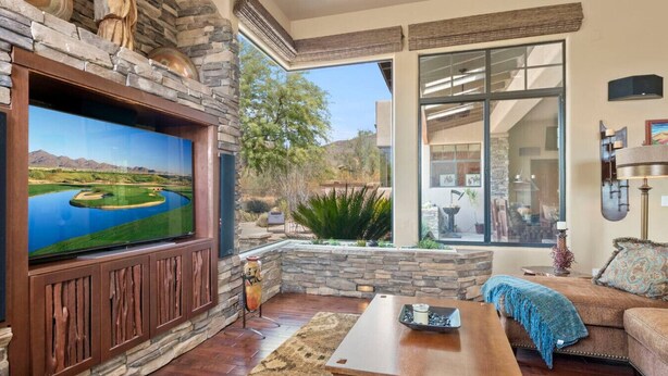 A living room with a stone fireplace, a large flat-screen TV, a wooden coffee table, and a sofa. - Gorgeous Desert Home W/ Backyard Oasis! (Cave Creek)