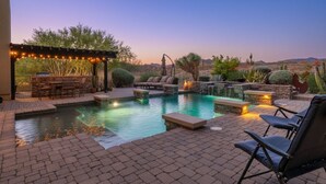 A pool area with lounge chairs, a pergola with string lights, and a stone wall with a water feature. - Gorgeous Desert Home W/ Backyard Oasis! (Cave Creek)