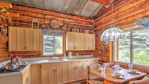 Una cocina de estilo rústico tipo cabaña, con armarios de madera, un ventanal grande y un comedor con mesa y sillas.