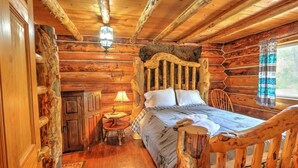 Un dormitorio de cabaña de madera con una cama de madera, una mesita de noche, una lámpara y una silla.