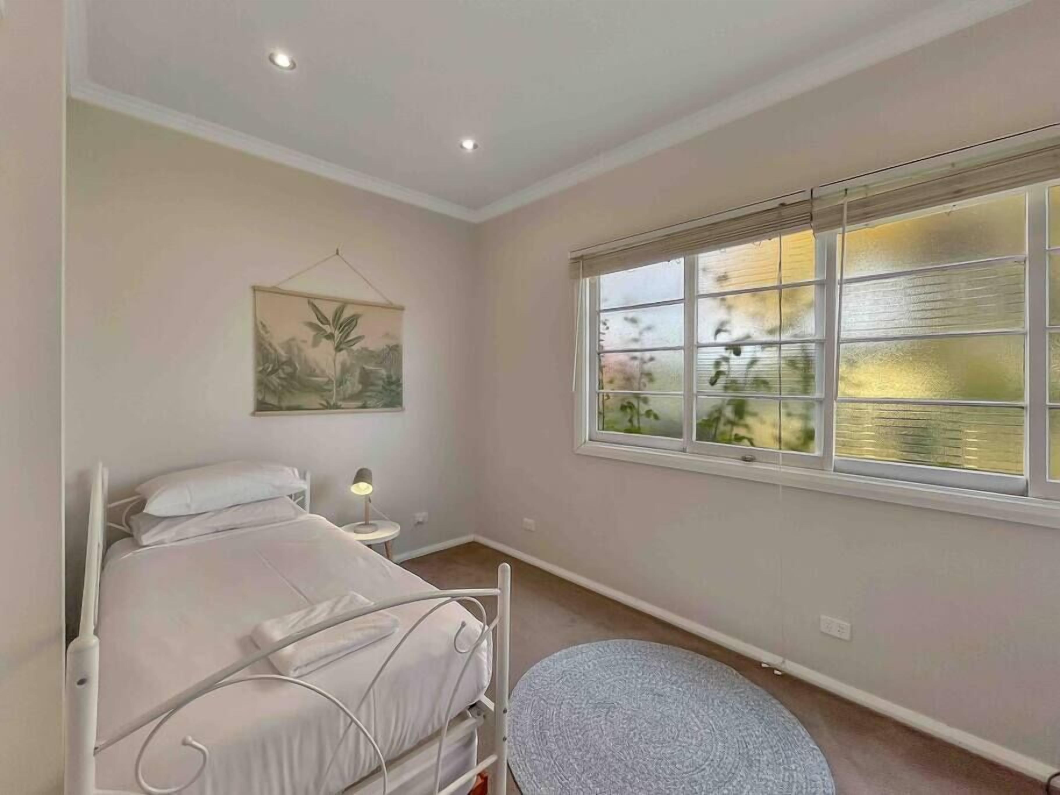 A bedroom with a bed, bedside table, lamp, and a window with a view of greenery.