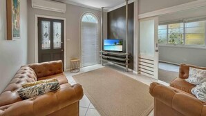A living room with two leather sofas, a flat-screen TV on a stand, a small round table, and a large window with blinds.