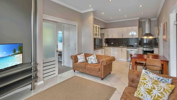 A modern living room with a sofa, a TV, and a kitchen in the background.