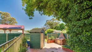 A fenced backyard with a small shed, a brick barbecue area, and a green fence. - Apt 3 Brightside Apartments - City Center (Armidale)