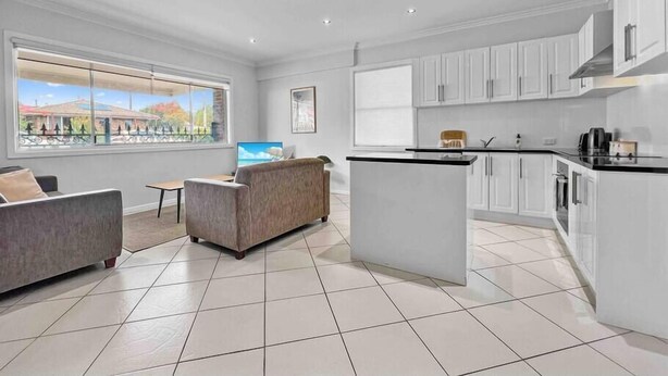 A modern kitchen with white cabinets, a central island, and a large window offering a view of a building and trees. - Apt 3 Brightside Apartments - City Center (Armidale)