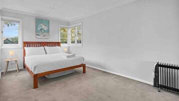 Un dormitorio con una cama de madera, dos mesitas de noche con lámparas y un radiador.