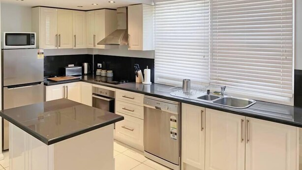 Una cocina moderna con armarios blancos, electrodomésticos de acero inoxidable, encimera negra y una ventana con persianas.