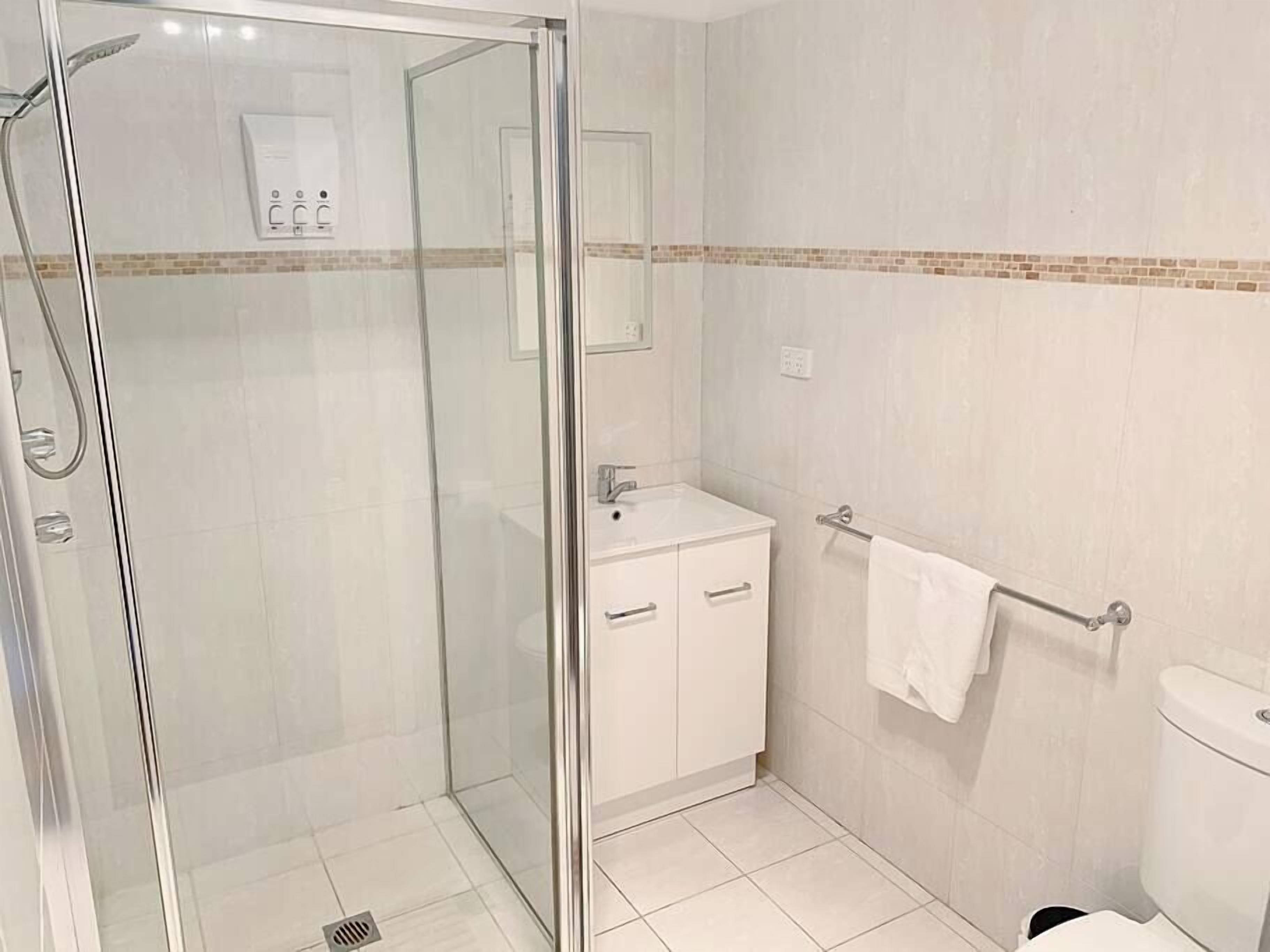 Une salle de bain moderne avec une douche à parois de verre, un lavabo blanc avec un miroir au-dessus et des toilettes dotées d’un porte-serviettes.