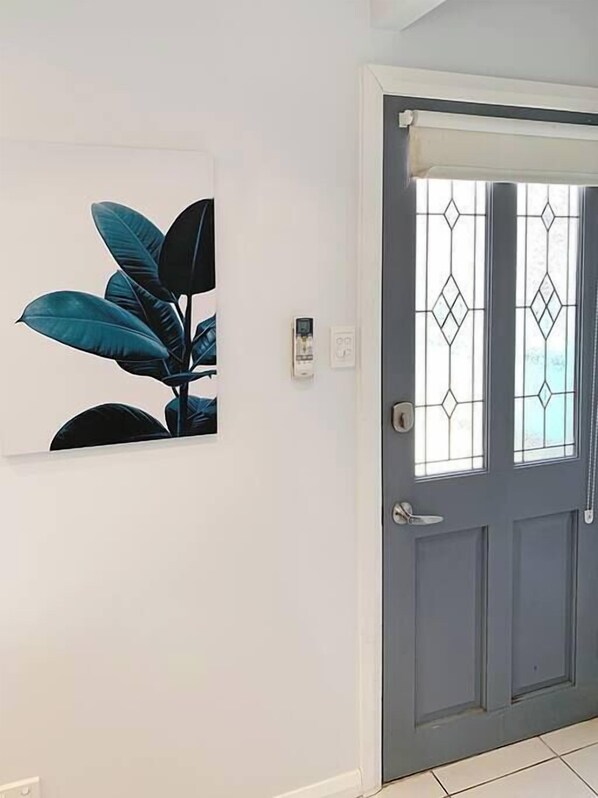 A door with a window, a wall-mounted light switch, and a framed picture of a plant.