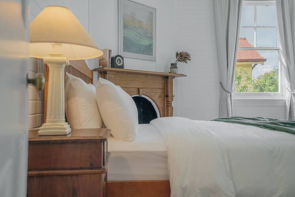 Une chambre à coucher avec un lit, une table de chevet avec une lampe, une cheminée et une fenêtre avec des rideaux.