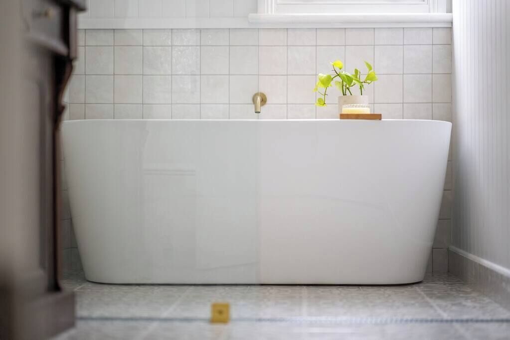 Une salle de bain moderne avec une baignoire sur pieds, une petite plante posée sur le bord et une fenêtre au-dessus de la baignoire.