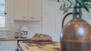 Een keuken met witte kastjes, een brood op een houten snijplank, en een vaas met een plant.