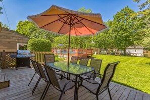A deck with a glass table and chairs, a barbecue grill, and a large umbrella.